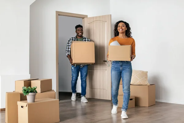 Real Estate Offer. Cheerful Black Couple Entering New House Carrying Moving Boxes At Home. Full Length Shot Of Spouses Coming Into Their Own House After Relocation. Housing For Young Family