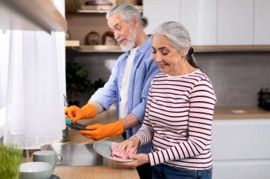 Portrait Of Smiling Senior Spouses Washing Dishes Together In Kitchen After Lunch, Happy Married Elderly Couple Cleaning Plates And Chatting, Sharing Domestic Chores Together, Copy Space