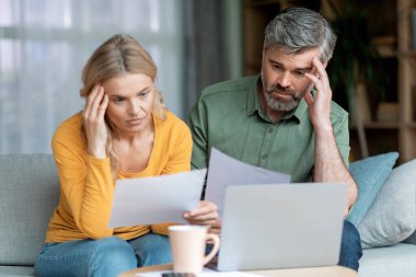 Financial Crisis. Pensive Middle Aged Couple Checking Documents At Home, Thoughtful Mature Spouses Sitting On Couch And Holding Papers, Suffering Problems With Managing Family Budget, Closeup Shot