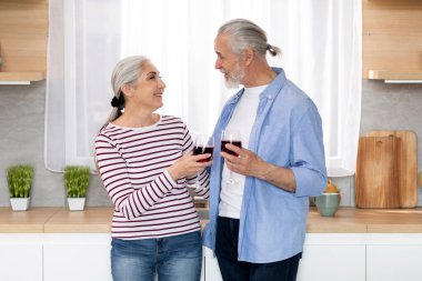 Happy Senior Spouses Drinking Wine And Chatting Together In Kitchen Interior, Portrait Of Smiling Romantic Elderly Man And Woman Having Drinks And Enjoying Spending Time At Home, Copy Space