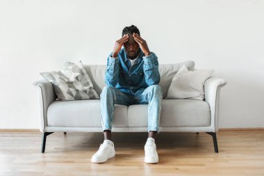 Male Depression. Unhappy Black Man Looking At Camera Having Problem Touching Head Sitting On Couch At Home. Millennial Man Thinking About Issues Having Bad Mood And Headache. Mental Health