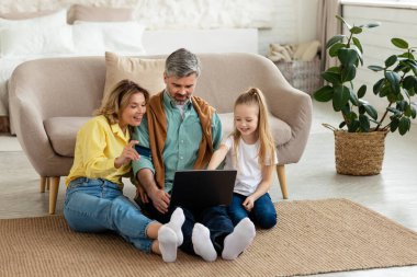 Online Shopping. Family Using Credit Card And Laptop Ordering Something On Internet And Making Payment Sitting On Floor In Modern Living Room At Home. Technology And Ecommerce