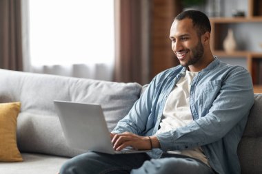 Remote Work. Handsome Young Black Freelancer Guy Using Laptop At Home, Smiling African American Male Working Online On Computer While Sitting On Comfortable Couch In Living Room, Copy Space