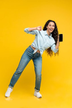 Great Application. Happy Middle Eastern Woman Showing Cellphone With Empty Screen Advertising Mobile App Standing Over Yellow Background. Vertical, Studio Shot