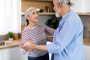 Portrait Of Loving Senior Couple Dancing Together In Kitchen Interior, Happy Romantic Elderly Spouses Having Fun, Holding Hands And Smiling To Each Other, Enjoying Spending Time At Home, Closeup Shot