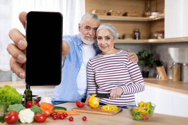 Mobile Ad. Smiling Senior Spouses Demonstrating Big Blank Smartphone In Kitchen At Home, Happy Elderly Man And Woman Showing Cellphone With Black Screen For Website Or App Design, Collage, Mockup