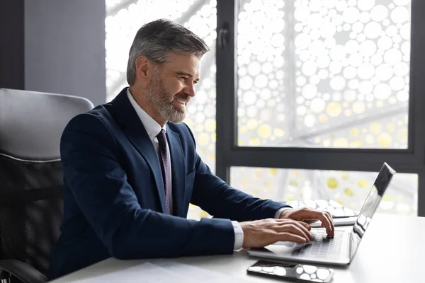 Successful Entrepreneurship. Handsome Middle Aged Businessman Working With Laptop In Office, Smiling Male Entrepreneur Sitting At Desk And Using Computer For Corporate Communication, Side View