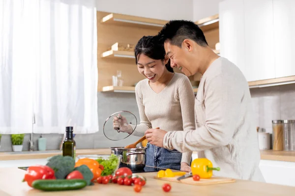 Cheerful japanese family middle aged husband and young wife enjoying cooking together at home, happy asian man and woman standing next to stove, preparing healthy dinner, copy space