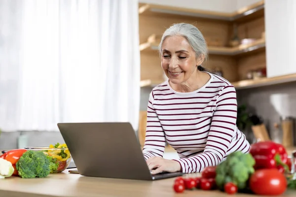 Portrait Smiling Elderly Lady Using Laptop Kitchen Happy Senior Woman — Stockfoto