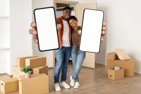 Happy Black Couple Standing Boxes Moving Showing Blank Smartphones White — Stok fotoğraf