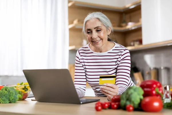 Happy Elderly Lady Using Laptop Credit Card While Cooking Lunch — Stockfoto
