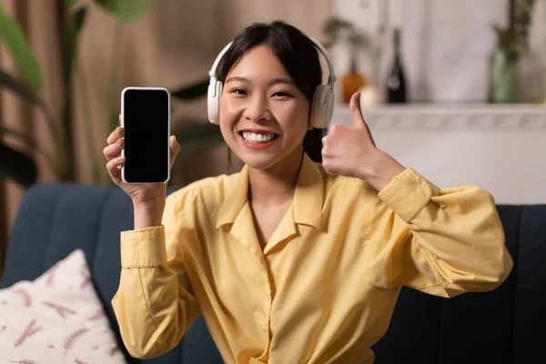 Happy Asian Woman Showing Smartphone Empty Screen Wearing Headphones Gesturing — ストック写真