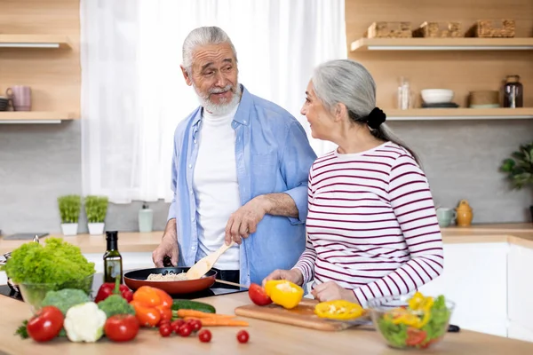 Happy Elderly Spouses Cooking Lunch Meal Together In Kitchen, Married Senior Couple Chatting While Preparing Healthy Food At Home, Old Man And Woman Enjoying Pastime On Retirement, Free Space