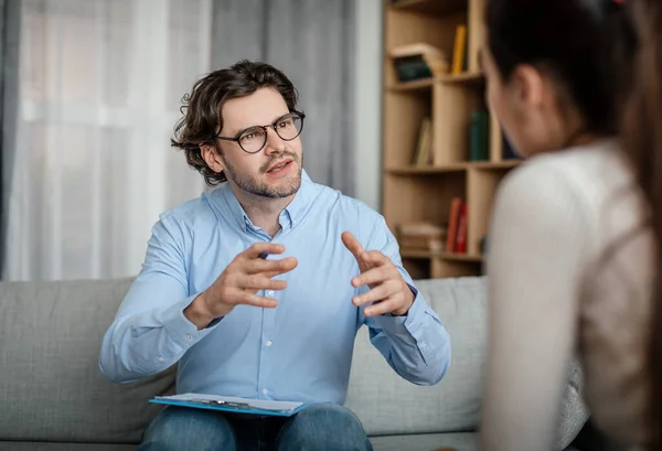 Emotional Young European Guy Doctor Speaks Gesticulates Woman Patient Office — Stockfoto
