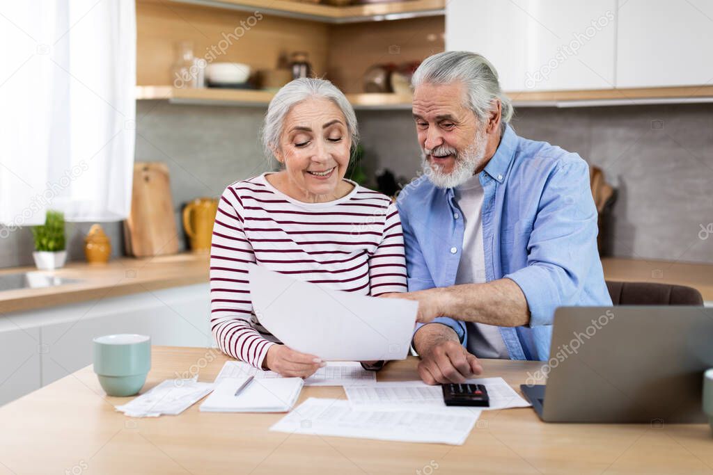 Financial Planning On Retirement. Portrait Of Happy Senior Couple With Laptop And Papers In Kitchen Discussing Family Budget Together, Elderly Spouses Calculating Spends And Taxes, Closeup Shot