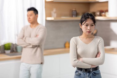 Selective focus on upset millennial asian woman in casual outfit having fight with boyfriend, kitchen interior. Sad korean spouses arguing at home, having difficulties in relationships