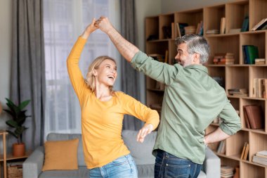 Portrait Of Positive Middle Aged Couple Dancing In Living Room Interior, Cheerful Mature Husband And Wife Having Fun At Home, Joyful Man And Woman Enjoying Spending Time Together, Free Space