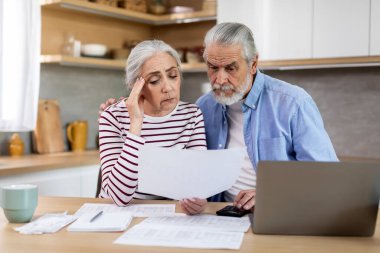 Portrait Of Upset Senior Spouses Reading Financial Papers While Calculating Family Budget In Kitchen, Married Elderly Couple Checking Their Loan Documents Or Bills Together At Home, Closeup