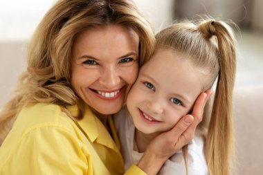 Portrait Of Loving Middle Aged Mother And Little Daughter Embracing Smiling To Camera Indoor. Mommy And Her Kid Posing Together At Home. Mothers Day, Family Lifestyle Concept