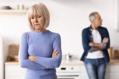 Selective focus on upset senior woman with arms crossed on chest looking aside, having quarrel with her husband, kitchen interior. Crisis in marriage for seniors, divorce at older ages concept