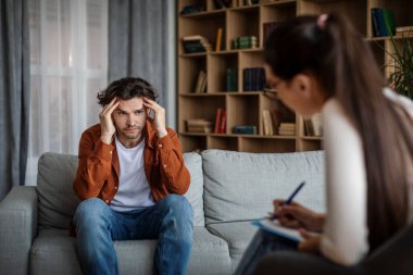 Despaired depressed young caucasian patient speaks with lady doctor psychologist in office clinic interior. Psychological therapy, medical support, personal consultation, treatment and mental problems