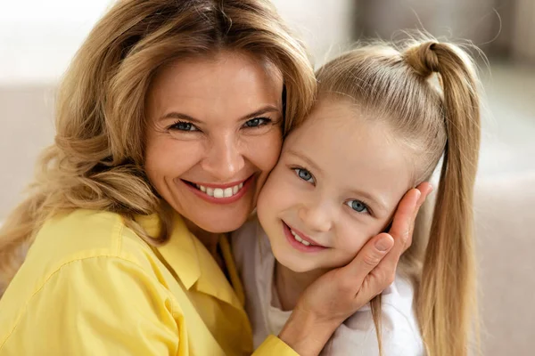 Portrait Of Loving Middle Aged Mother And Little Daughter Embracing Smiling To Camera Indoor. Mommy And Her Kid Posing Together At Home. Mothers Day, Family Lifestyle Concept