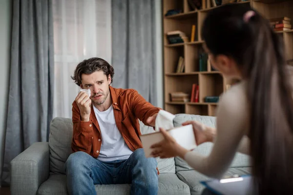 Professional help, advice and consultation. Caucasian young female psychologist calms crying man patient in clinic interior. Stress, pressure, mental problems, medical care, fight against depression