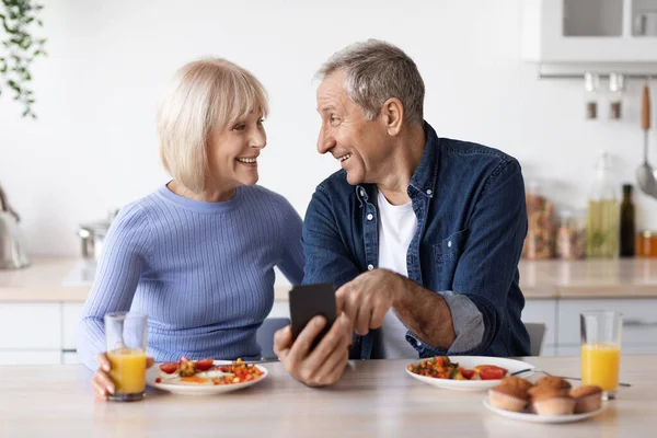 Smiling Senior Spouses Having Delicious Healthy Breakfast Together Using Cell — Stockfoto