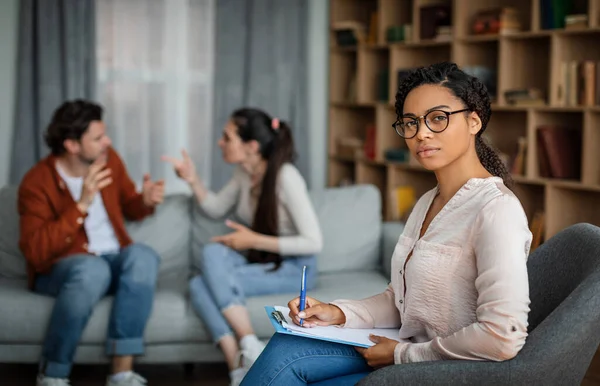 Angry emotional young european couple quarreling at meeting with african american psychologist in office clinic interior. Family psychological therapy, mental treatment, professional help and business