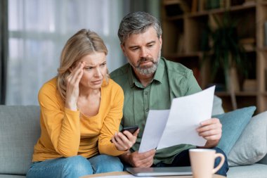 Budget Planning. Stressed Middle Aged Spouses Holding Papers And Calculating Family Spends Together, Thoughtful Mature Spouses Checking Documents, Suffering Financial Crisis, Closeup Shot