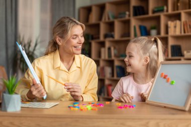 Child development school. Professional female teacher exercising with preschool girl, happy little child making mathematical equations on a magnetic board