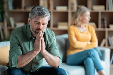Marriage Problems. Portrait Of Middle Aged Wife And Husband Upset After Quarrel At Home, Offended Mature Spouses Ignoring Each Other, Suffering Relationship Crisis, Selective Focus At Pensive Man