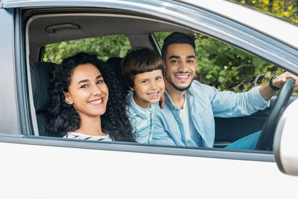 Happy millennial middle eastern family with child go to vacation by car and look at camera, copy space. Family trip on new auto, weekend together, love and relationship, journey and facial expression