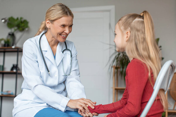 Pretty schoolgirl having appointment with friendly professional female pediatrician at modern clinic, copy space. Modern healthcare for children concept