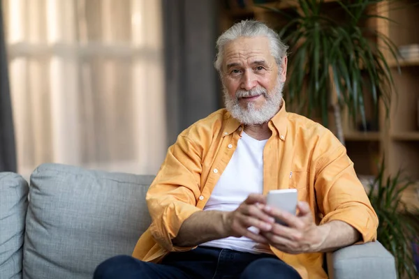 Cheerful Elderly Man Sitting Couch Home Using Modern Cell Phone — Stok fotoğraf