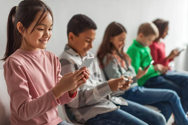 Diverse School Children Using Phones Playing Mobile Games Online Sitting — стоковое фото