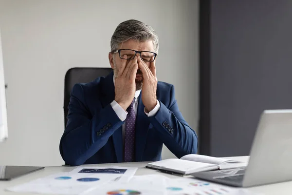 Business Stress. Portrait Of Tired Middle Aged Businessman Rubbing Eyes In Office, Exhausted Mature Male Entrepreneur Sitting At Desk And Massaging Nose Bridge, Suffering Overwork, Closeup Shot