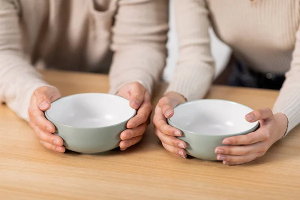 Unrecognizable people husband and wife sitting at kitchen table with empty bowls, hungry family has nothning to eat, suffering from hunger while crisis during coronavirus pandemic, cropped