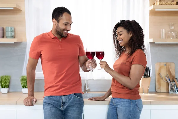 Smiling young african american man and woman in same t-shirts with glasses of wine enjoy free time together, celebrate anniversary, holiday in kitchen interior. Relationships, love, romance at home