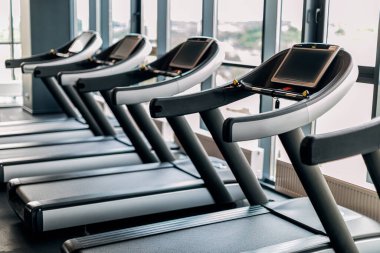 Sport Equipment. Modern Treadmills With Control Panels Standing In A Row At Gym Interior, Closeup Shot Of Training Tools For Running Placed Near Panoramic Windows In Fitness Club Without Visitors