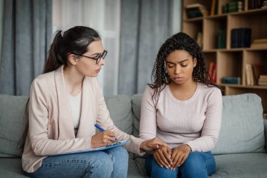 Calm european lady calms sad black millennial woman, doctor consultation patient in clinic interior. Medical support, professional consultation, patient care, depression therapy and mental problems