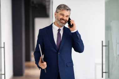Smiling Middle Aged Businessman Talking On Cellphone While Walking Out Of Office, Happy Male Entrepreneur Wearing Suit Holding Laptop In Hand And Having Pleasant Business Call, Copy Space