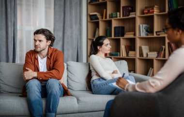 Quarrel and scandal. Sad caucasian millennial husband ignores woman on consultation with psychologist in clinic interior. Professional medical care, family relationships, mental problems and stress