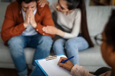Depression treatment. Unhappy caucasian woman calms crying man on consultation with psychologist in clinic interior, cropped, blurred. Medical care, family relationships, mental problems and help