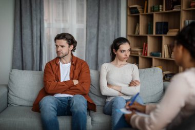 Angry millennial caucasian woman ignores man on consultation with psychologist in clinic interior. Human emotions, medical care, family relationships, solving mental problems, quarrel and stress