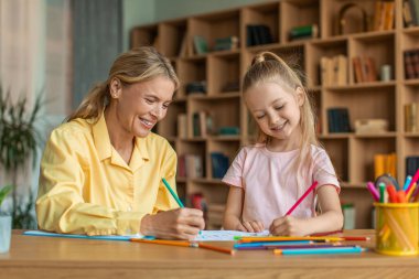 Creativity lessons for children. Happy cute girl drawing with professional female teacher at cabinet, enjoying art classes at private preschool lessons