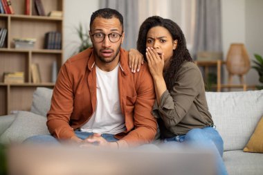 Bad News. Shocked African American Couple Watching Shocking TV Content Sitting On Sofa At Home. Weekend Leisure, Television Programming Concept. Selective Focus