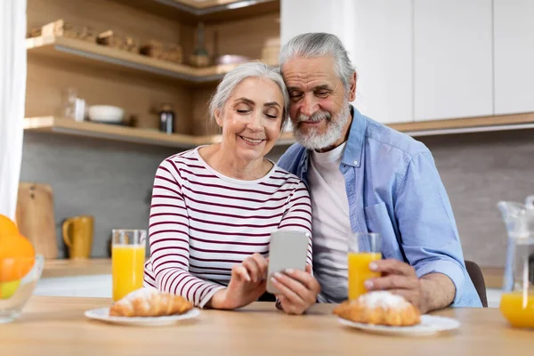 Happy Senior Spouses Spending Time Smartphone While Having Breakfast Kitchen — Stockfoto