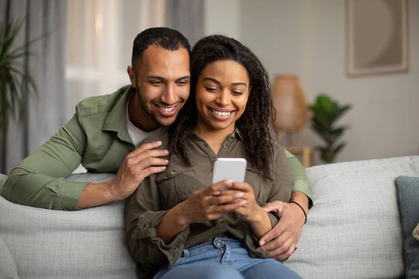 Happy Black Spouses Using Cellphone Texting Husband Embracing Wife Browsing — Stok Foto