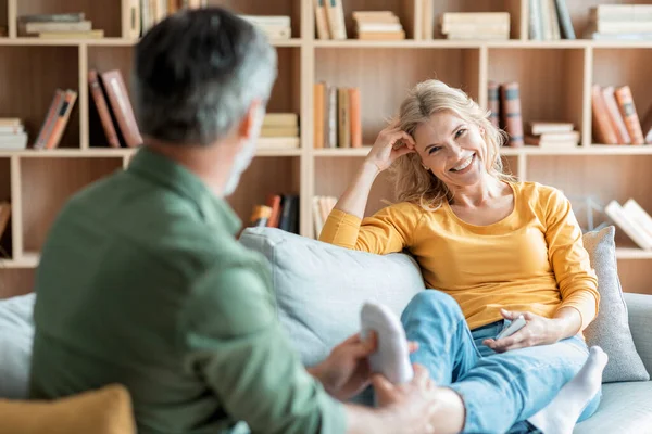 Caring Man Massaging Feet Toes Of His Wife While They Relaxing On Couch In Living Room, Happy Middle Aged Couple Resting Together In Cozy Home Interior, Enjoying Domestic Leisure, Selective Focus